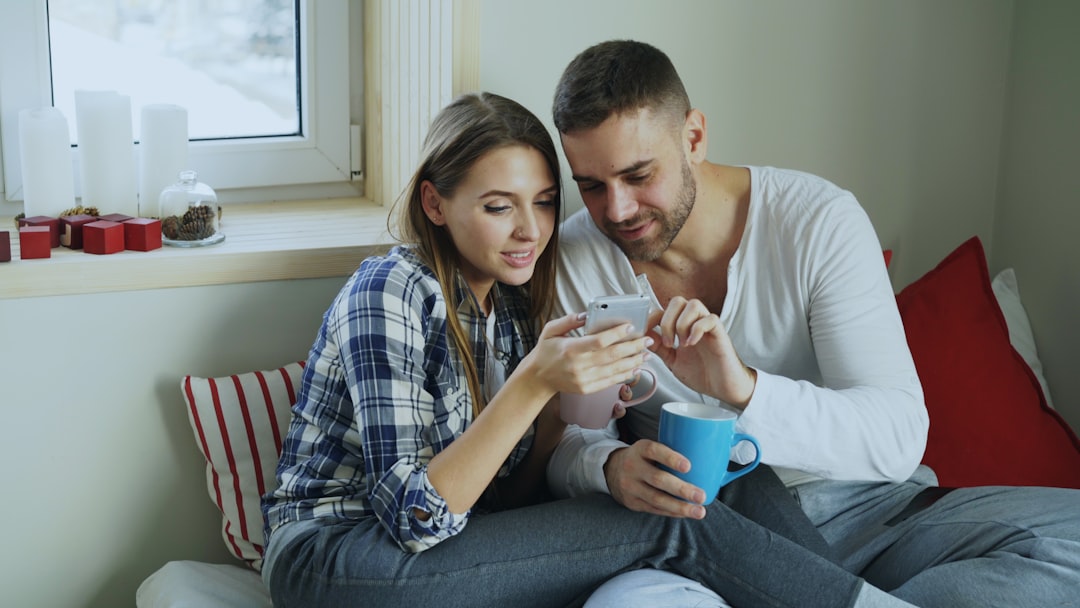 A smiling couple looks relieved and happy as they hold up house keys inside their bright, modern, and minimally decorated living room.
