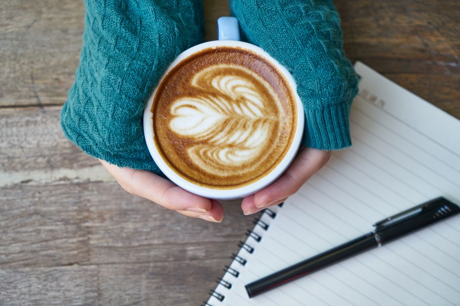 A close-up of a person's hands holding a warm coffee mug, creating a calm focal point in a blurred background of a room being packed up for a move.