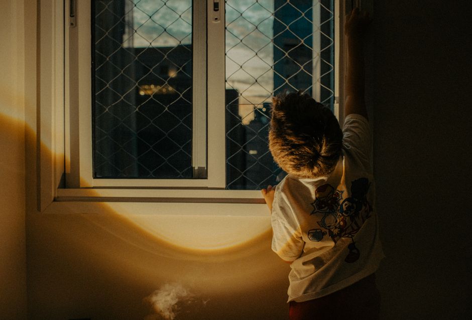 A person stands in silhouette looking out a large window in a bright, empty room, symbolizing the feeling of letting go and the uncertainty of moving.