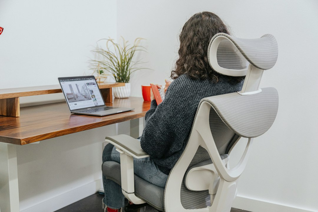 A professional sits at a clean, modern desk in a calm office, thoughtfully looking at a laptop screen, representing a therapist planning their marketing strategy.